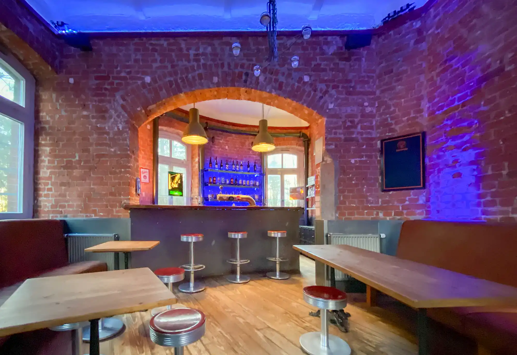 IMG 5335 Innenraum einer Bar mit roten Backsteinwänden, gemütlichen Sitzbänken und kleinen Tischen, stilvolle Beleuchtung und eine gut ausgestattete Bar im Hintergrund, ideal für entspannte Abende und gesellige Treffen.