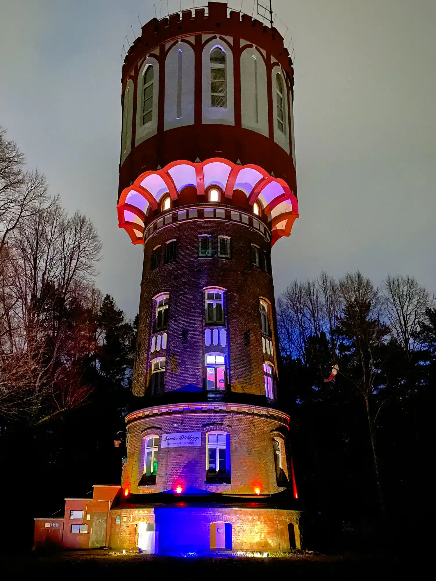 Farblich beleuchteter Turm, historisches Wahrzeichen, nachts, im Wald, mit bunten Lichter, Attraktion, Touristenattraktion, festliche Beleuchtung, am Wasser, kreative Lichtgestaltung, außergewöhnliches Bauwerk.