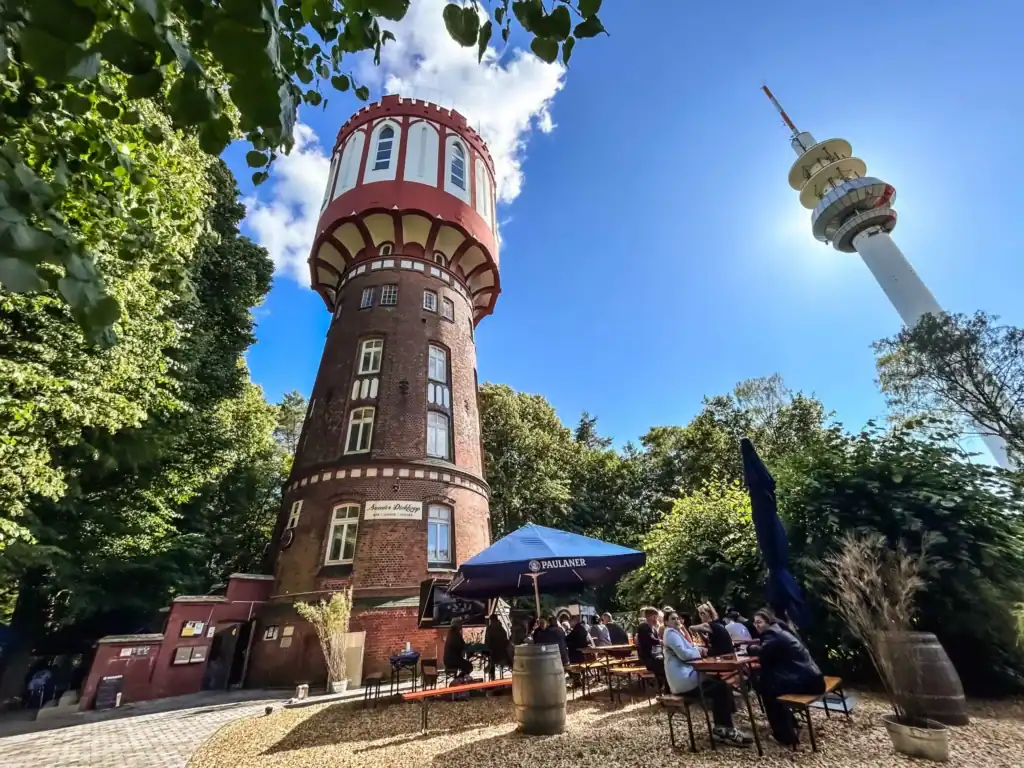 Historischer Wasserturm und Fernsehturm in einer grünen Parklandschaft, perfekt für ein Treffen im Freien, mit blauen Himmel und sonnigem Wetter.