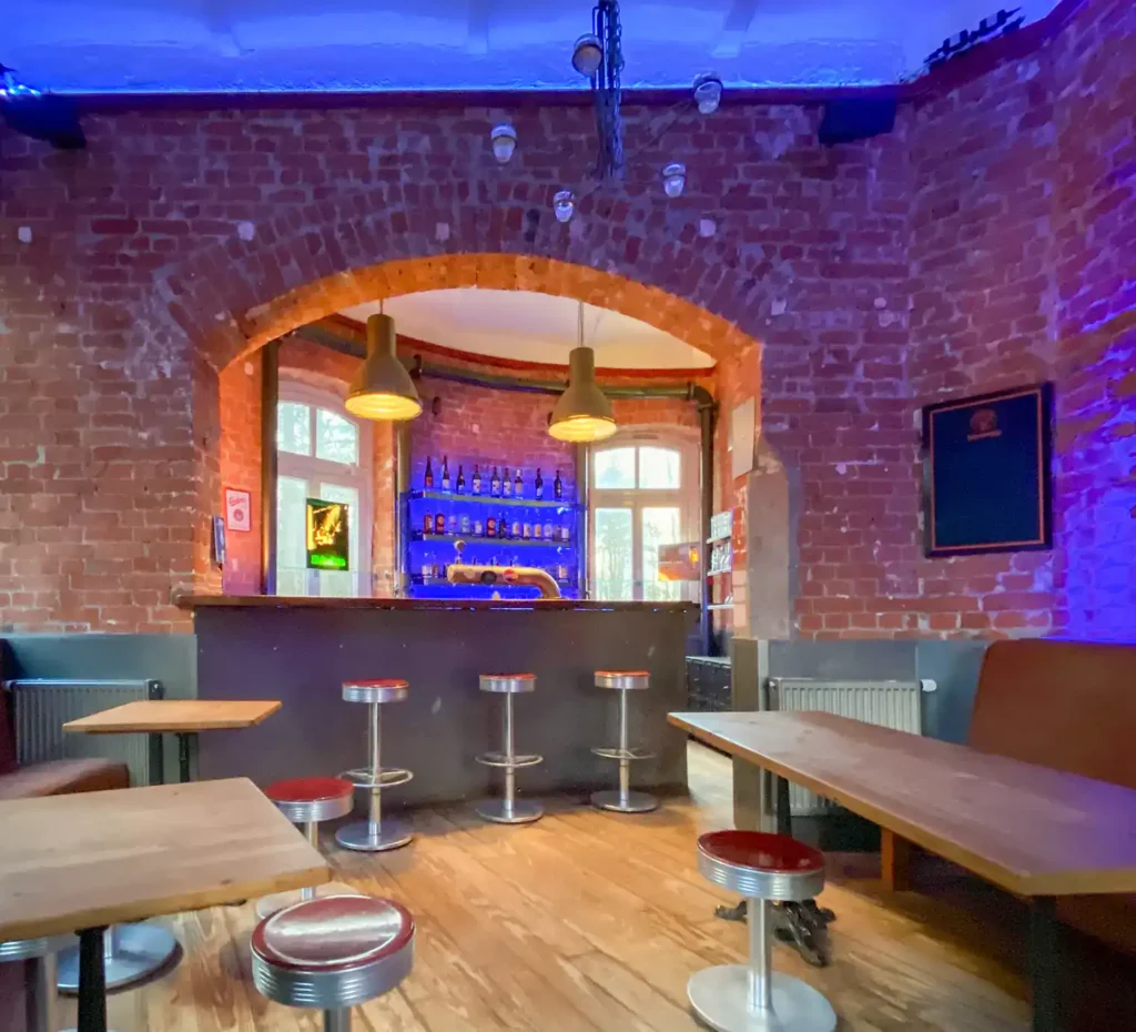 IMG 5335 Innenraum einer Bar mit roten Backsteinwänden, gemütlichen Sitzbänken und kleinen Tischen, stilvolle Beleuchtung und eine gut ausgestattete Bar im Hintergrund, ideal für entspannte Abende und gesellige Treffen.